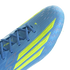 A close-up of a light blue Adidas F50 soccer cleat featuring three bold neon yellow stripes on the side. The shoe has a textured, ribbed upper with blue laces and a shimmering checkered pattern near the toe, shown against a black background.