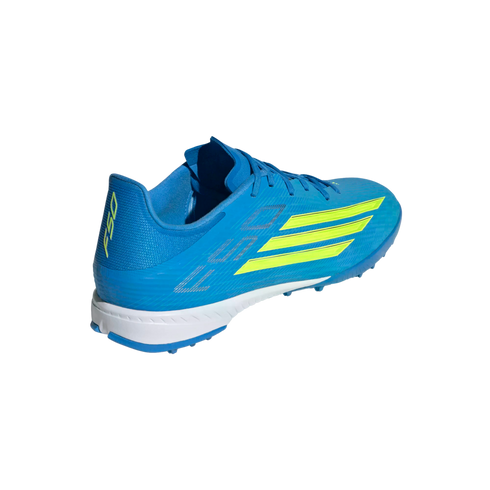 A rear three-quarter view of a bright blue Adidas F50 turf soccer shoe with neon yellow stripes and a white midsole.