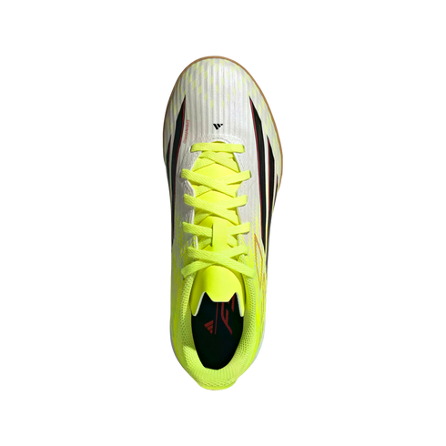 Top-down view of a white Adidas indoor soccer shoe with neon yellow laces and collar, featuring black and red accents on a solid black background.
