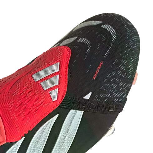 Close-up of a black and red Adidas Predator soccer cleat featuring a textured "NANOSTRIKE+" upper, red fold-over tongue with silver stripes, and a black "PREDATOR" strap.