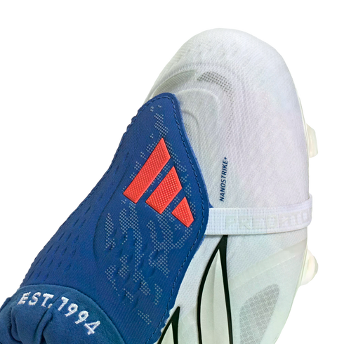 White and blue Adidas soccer cleat featuring a blue tongue with a red logo and white "EST. 1994" embroidery against a black background.