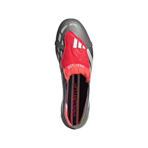 Top-down view of a grey and red Adidas Predator soccer cleat with a red fold-over tongue featuring "EST. 1994" and "PREDATOR" printed on the insole, set against a black background.