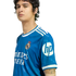 Young man wearing a blue Real Madrid soccer jersey with white trim and sponsor logos, posed against a black background.