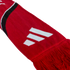 A red knitted scarf featuring a white three-stripe logo, a black and white curved stripe, and red tassels at the end.