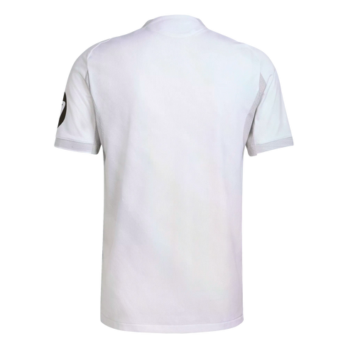 Back view of a white short-sleeved sports shirt with a subtle textured mesh and a black circular logo on the left sleeve, isolated on a white background.