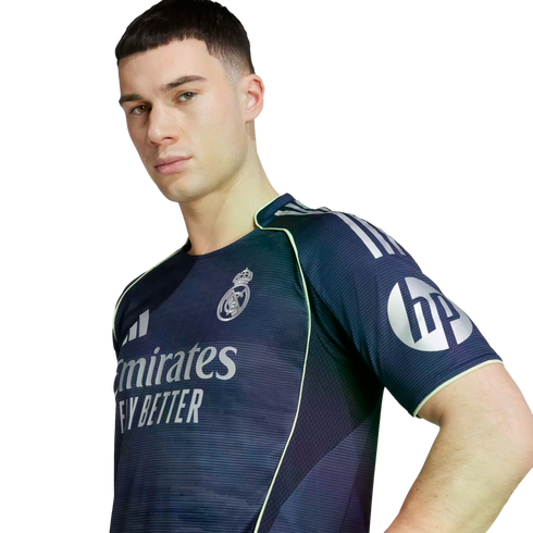 Young man wearing a navy Real Madrid training jersey with silver logos and neon green trim, posing against a white background.