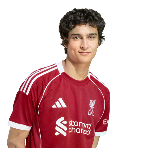 A young man with wavy dark hair wearing a red Liverpool F.C. soccer jersey against a solid black background.
