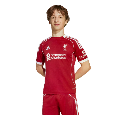 Young man wearing a red Liverpool FC soccer kit with white details and sponsor logos, standing against a solid black background.