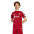 Young man wearing a red Liverpool FC soccer kit with white details and sponsor logos, standing against a solid black background.