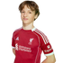 Young person with wavy brown hair wearing a red Liverpool F.C. jersey against a black background.