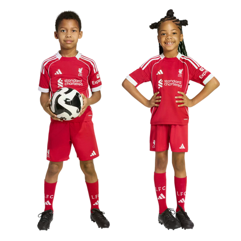 Two children wearing red Liverpool FC football kits. A boy holds a soccer ball while a girl smiles with her hands on her hips.