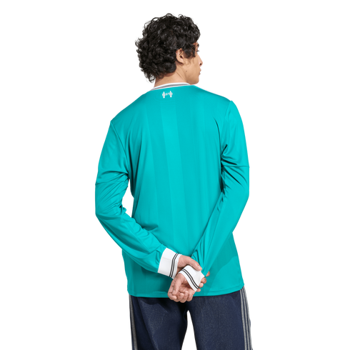 Back view of a person in a long-sleeved teal athletic jersey with white striped trim, standing with hands behind their back on a white background.