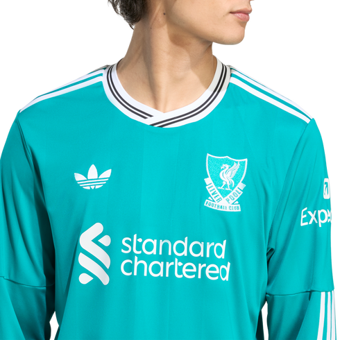 A person wearing a teal Liverpool FC long-sleeve jersey featuring white Adidas, Standard Chartered, and Expedia logos against a white background.