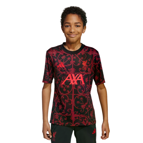 A young boy wearing a red and black patterned Liverpool FC training jersey, smiling against a solid black background.