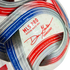 Close-up of a white MLS PRO soccer ball with red and blue stripes, the commissioner’s signature, and geographic coordinates printed on the surface.