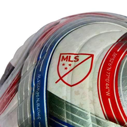 Close-up of an MLS soccer ball featuring the red league logo and geographic coordinates printed along curved blue and red stripes on a white textured surface.