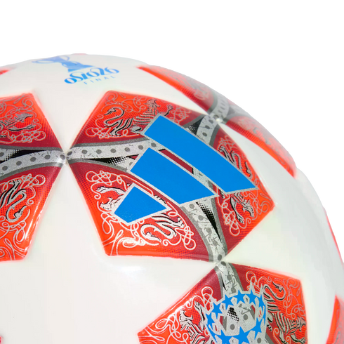 A close-up of a white Adidas soccer ball with orange star-shaped panels featuring intricate silver patterns and a prominent blue logo.