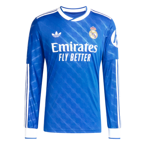 Long-sleeved blue Real Madrid jersey with white Adidas Trefoil, team crest, and Emirates sponsor. Features white collar and cuffs with subtle tonal patterns.