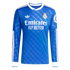 Long-sleeved blue Real Madrid jersey with white Adidas Trefoil, team crest, and Emirates sponsor. Features white collar and cuffs with subtle tonal patterns.