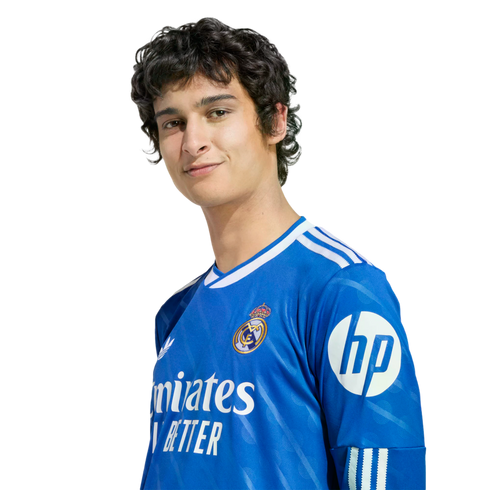 A headshot of soccer player Alvaro Rodriguez smiling, wearing a blue Real Madrid jersey with sponsor logos.
