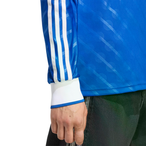 Blue long-sleeve shirt with three white stripes on the sleeve, white cuffs, and a diagonal pattern. Hand and dark pants are visible.
