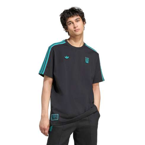 A man in a black Adidas x Liverpool FC tee with teal accents and logos, wearing black joggers, against a solid black backdrop.