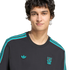 A man with dark wavy hair wearing a charcoal sweatshirt with teal shoulder stripes, a teal Adidas Trefoil logo, and a teal Liverpool FC crest on the chest.