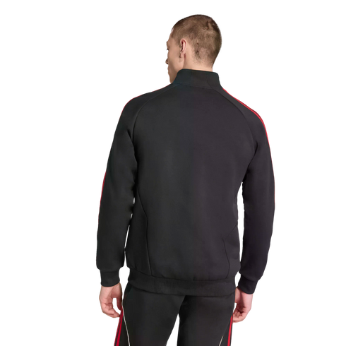 Rear view of a man wearing a black tracksuit with red stripes along the shoulders and pants, standing against a solid black background.