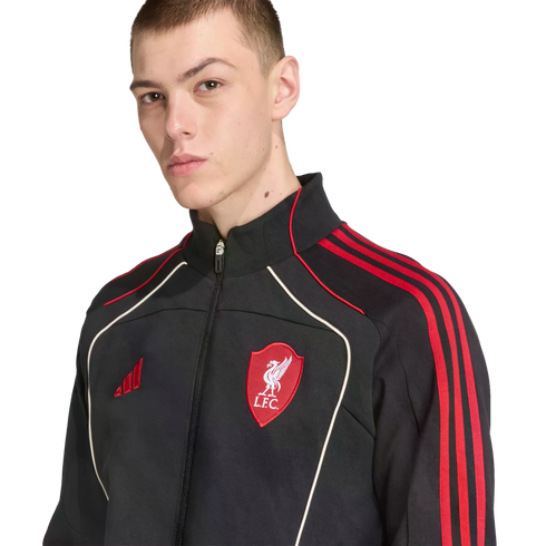 A man wearing a black Adidas Liverpool F.C. track jacket with red stripes and white piping, set against a black background.