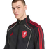 A man wearing a black Adidas Liverpool F.C. track jacket with red stripes and white piping, set against a black background.