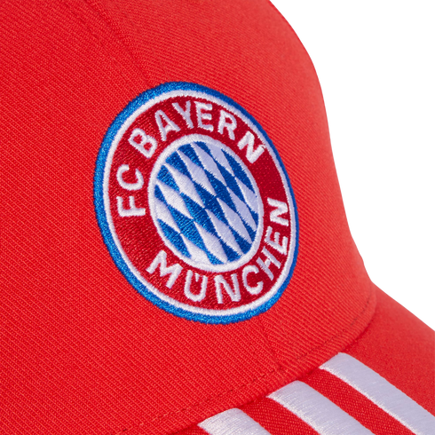 Close-up of a red baseball cap featuring the embroidered FC Bayern Munich circular crest and white stripes on the brim.