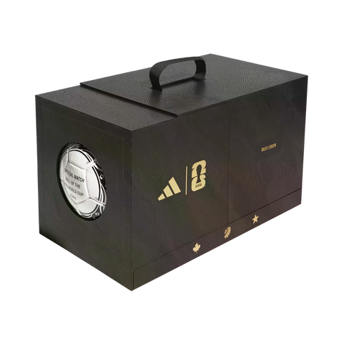 A black commemorative box with gold Adidas and FIFA World Cup 26 logos, host nation icons, and a window displaying a 1994 official match ball.