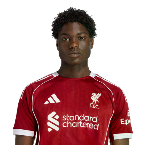 A headshot of a young Black man with curly hair wearing a red Liverpool F.C. jersey against a solid black background.