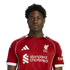 A headshot of a young Black man with curly hair wearing a red Liverpool F.C. jersey against a solid black background.