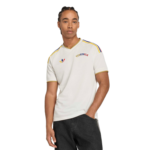 A man in a white Adidas Venezuela jersey with colorful shoulder stripes and gold trim, posed against a black background.
