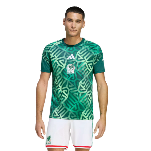 Male model wearing a Mexico national football team kit by Adidas, featuring a green geometric patterned jersey and white shorts.
