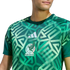 A man wears a green Adidas Mexico soccer jersey featuring a bold, geometric pattern inspired by ancient civilizations and the official team crest.