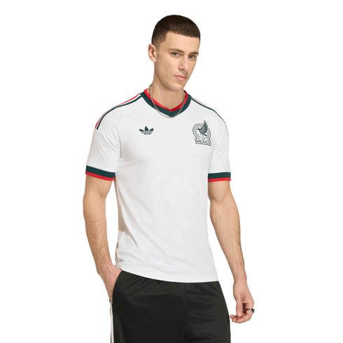 Man in a white Adidas Mexico soccer jersey with green and red trim, black shorts, and a silver chain against a black background.