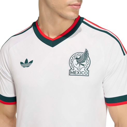 Close-up of a white Mexico national team soccer jersey featuring green and red trim, the team crest, and a green Adidas logo.