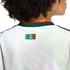 A person with dark curly hair from behind, wearing a white Mexico national team jersey. On the upper back, just below the green and red collar, is a small rectangular logo that reads "SOMOS MÉXICO" in the colors of the Mexican flag.