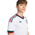 A young man wearing a white Mexico football jersey with green and red trim, an Adidas logo, and team crest, set against a black background.