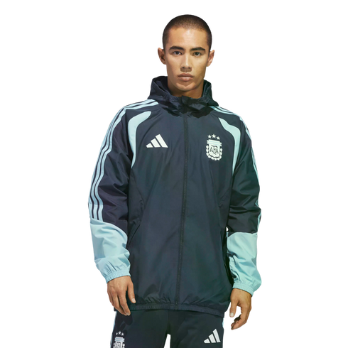 Man wearing a navy and light blue Adidas Argentina national football team windbreaker and matching pants with the AFA crest, against a black background.
