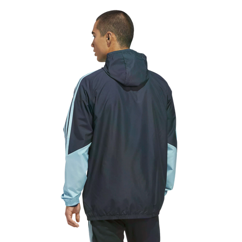 Man from the back wearing a navy blue and light blue hooded windbreaker jacket against a black background.