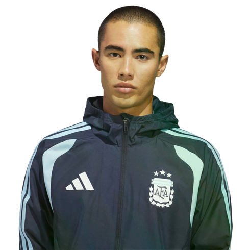 A man with a buzz cut wearing an Adidas Argentina national football team zip-up jacket against a black background.