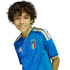Smiling boy with curly brown hair wearing a blue Italy soccer jersey against a black background.