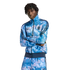 A person with dreadlocks poses in a blue tie-dye Adidas tracksuit featuring a "QUAKES" crest, set against a solid black background.