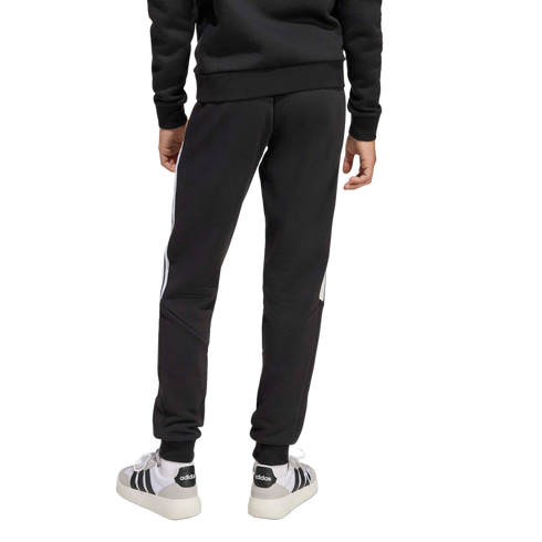 Rear view of a person wearing a black sweatshirt, black Adidas sweatpants with white side stripes, and white Adidas sneakers against a plain light grey background.