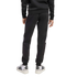 Rear view of a person wearing a black sweatshirt, black Adidas sweatpants with white side stripes, and white Adidas sneakers against a plain light grey background.