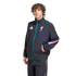 A person with curly brown hair models a black Adidas Liverpool F.C. track jacket featuring teal and pink accents, standing against a solid black background.