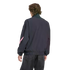 Rear view of a person with wavy brown hair wearing a dark navy zip-up jacket with a pink design on the sleeve and black jeans, set against a black background.